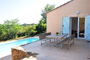 Une terrasse extérieure avec une piscine, une table et des bancs.