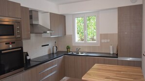 A modern kitchen with stainless steel appliances, wooden cabinets, a large window, and a wooden table. - Hillside Villa with Pool, Joyeuse (Joyeuse)