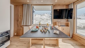 Een moderne eethoek met een grote tafel voor vier personen, houten wandbekleding, een flatscreen-tv en uitzicht op een besneeuwde berg.