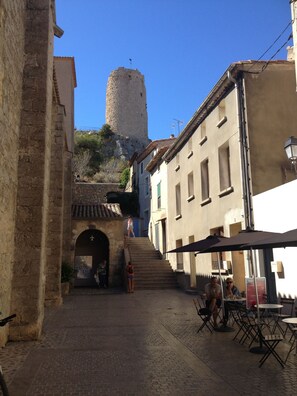 Un vicolo stretto con edifici in pietra, una torre e posti a sedere all'aperto.
