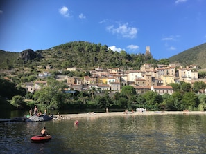 A coastal village with buildings on a hillside, a river in the foreground, and people engaging in water activities. - Mobile home 40m2 8persons (Valras plage)