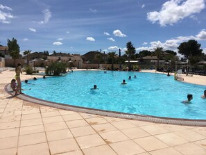 A large outdoor swimming pool surrounded by lounge chairs and umbrellas, with a clear sky above.
