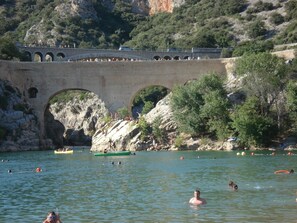 Un ponte di pietra che sovrasta un corso d'acqua, con persone che nuotano e barche.