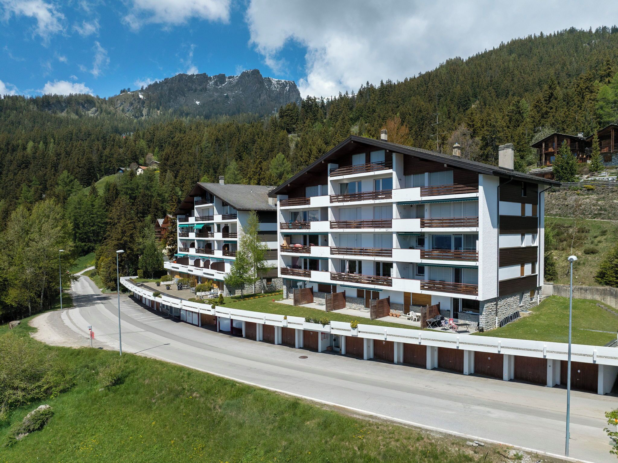 Ein mehrstöckiges Hotel mit Balkonen, eine Straße im Vordergrund und eine gebirgige Kulisse.