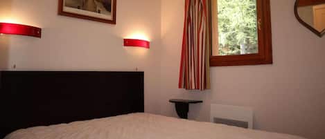 A bedroom with a bed, a nightstand, a framed picture, a window with curtains, and a mirror on the wall.
