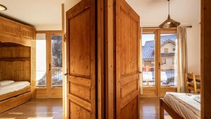 A wooden room with a bed, a wooden wardrobe, and a window with a view of buildings. - 300m from ski lifts, fitness, sauna, hammam, balcony, fireplace or stove, ski locker, 120m² (Valloire)