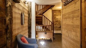 A narrow hallway with wooden walls, a blue chair with a red cushion, and a staircase leading to another level. - 300m from ski lifts, fitness, sauna, hammam, balcony, fireplace or stove, ski locker, 120m² (Valloire)