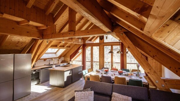 A spacious attic room with a high ceiling and wooden beams, featuring a kitchen, dining area, and seating space. - 300m from ski lifts, fitness, sauna, hammam, balcony, fireplace or stove, ski locker, 120m² (Valloire)