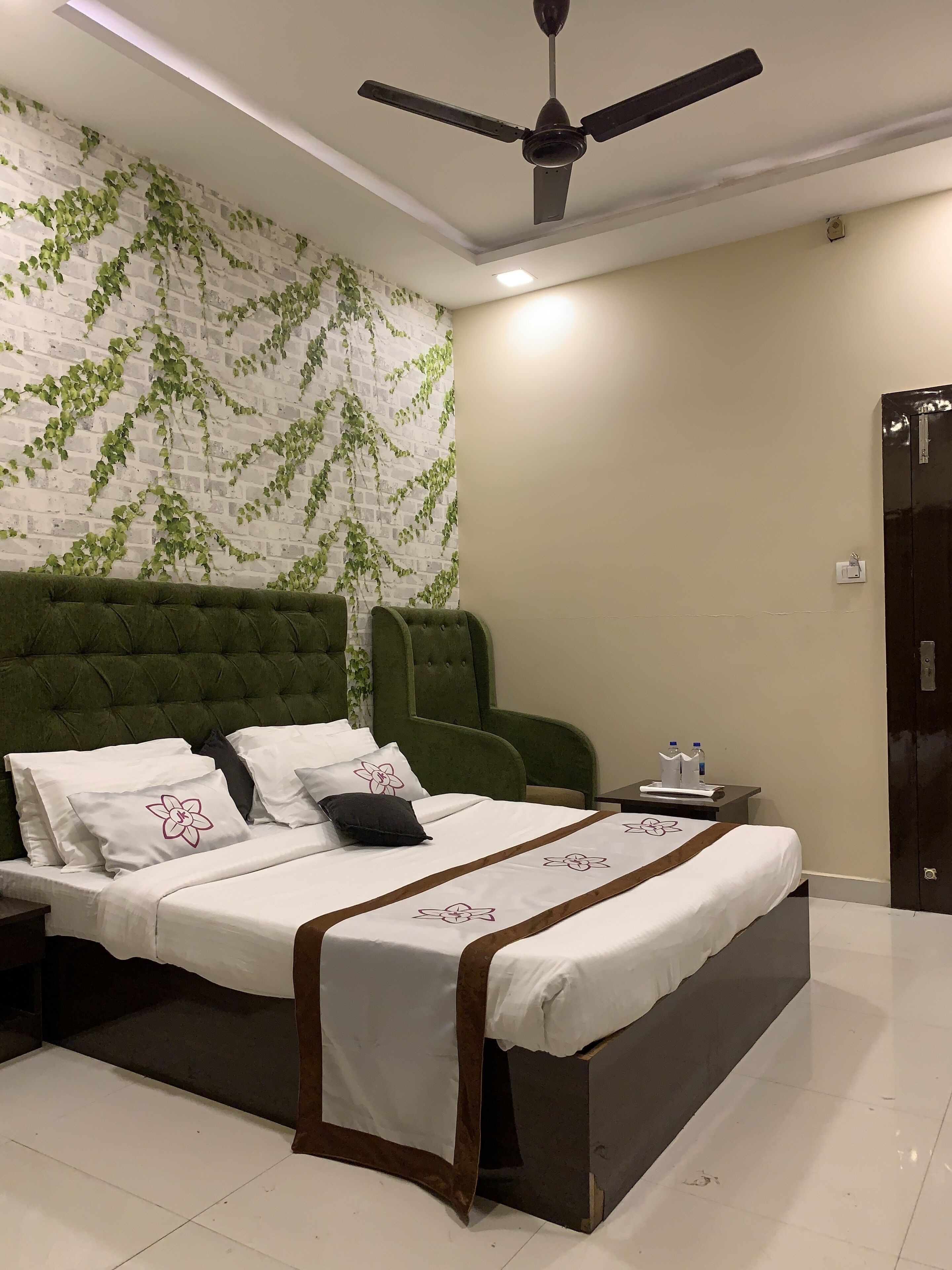 Een netjes ingerichte hotelkamer met een bed, een met groen bekleden hoofdeinde en een plafondventilator.