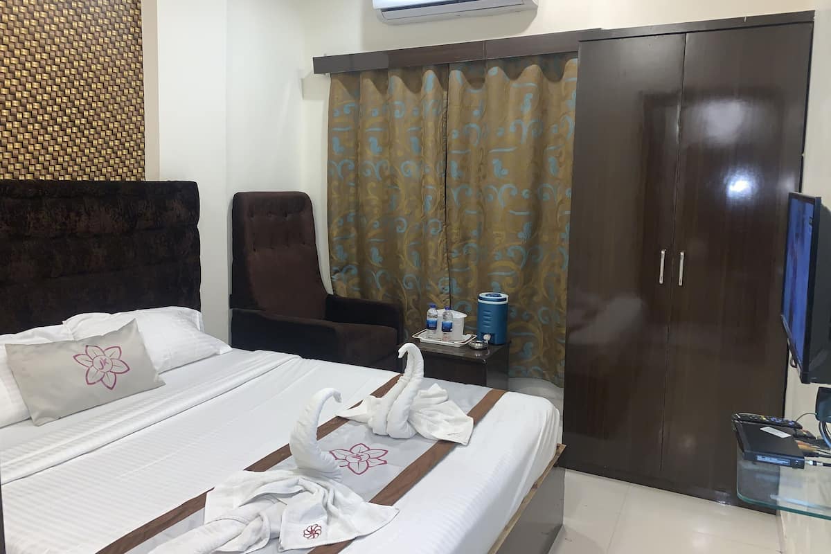 Een hotelkamer met een bed, een stoel, een kledingkast, een airconditioningsysteem en een televisie.