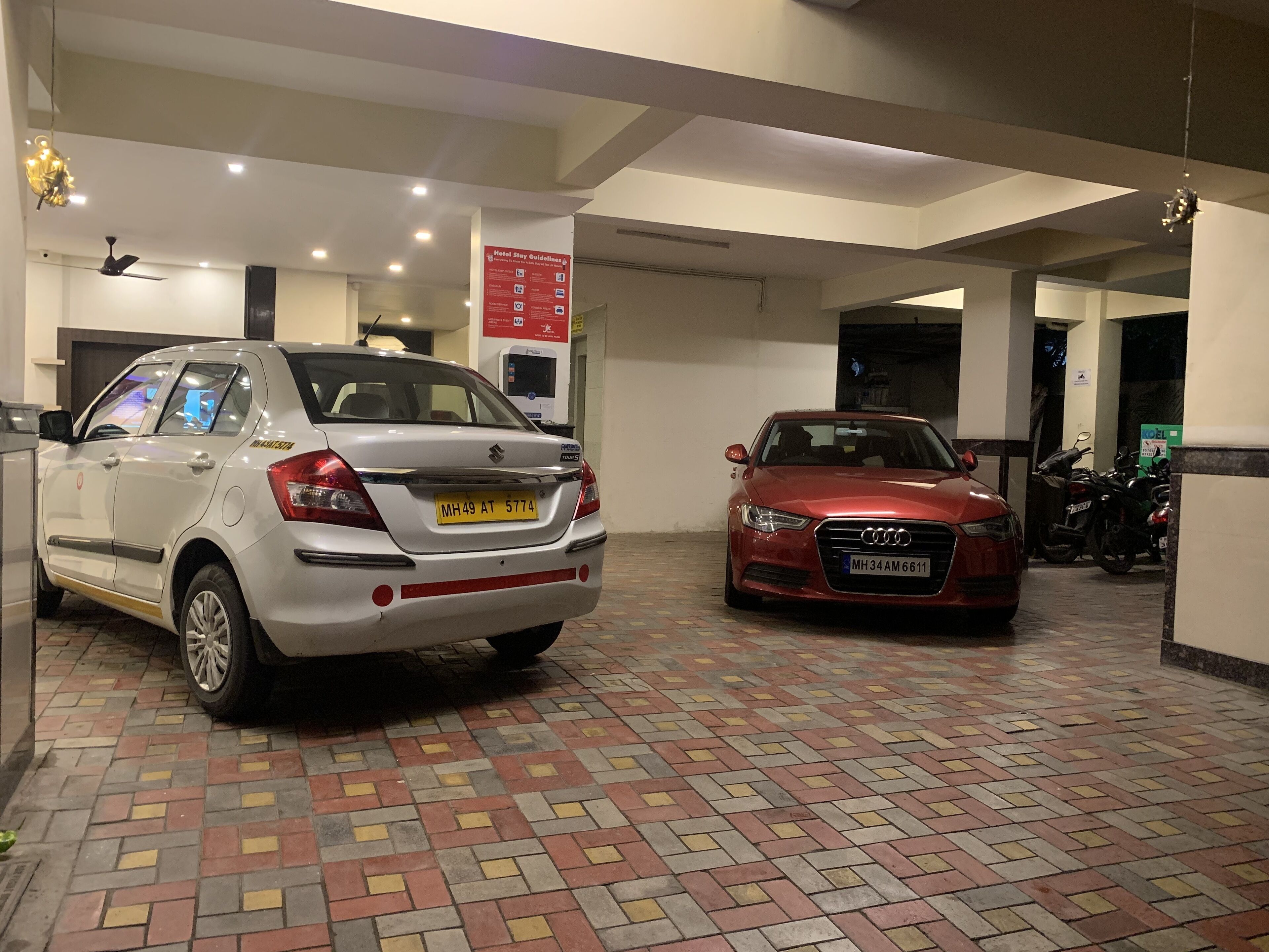 Ein Hotelparkplatz mit zwei Autos, einem weißen Suzuki und einem roten Audi, und einem gemusterten Boden.