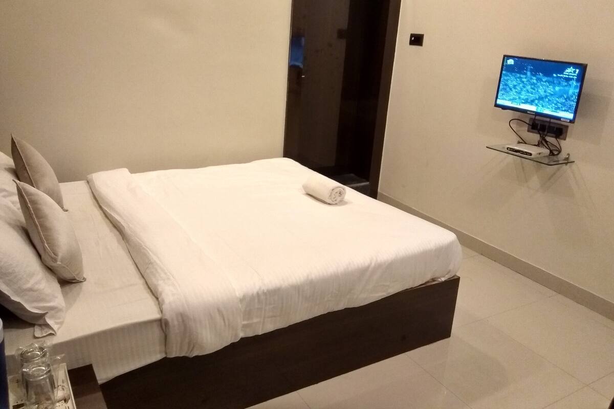 Een moderne hotelkamer met een netjes opgemaakt bed, een flatscreen televisie aan de wand en een schoon, minimalistisch design.