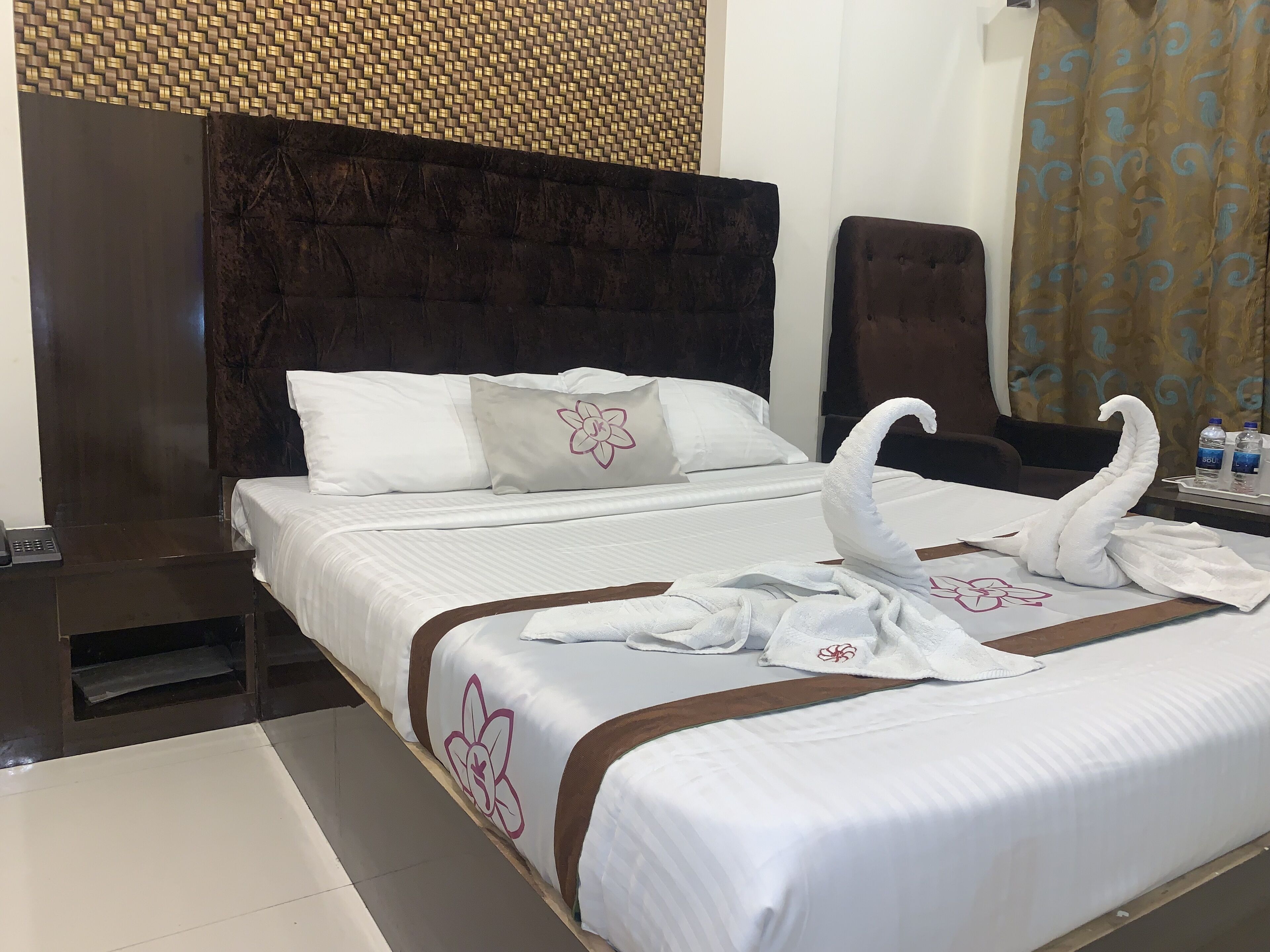 A hotel room with a large bed, a dark headboard, and a woven wall decoration.