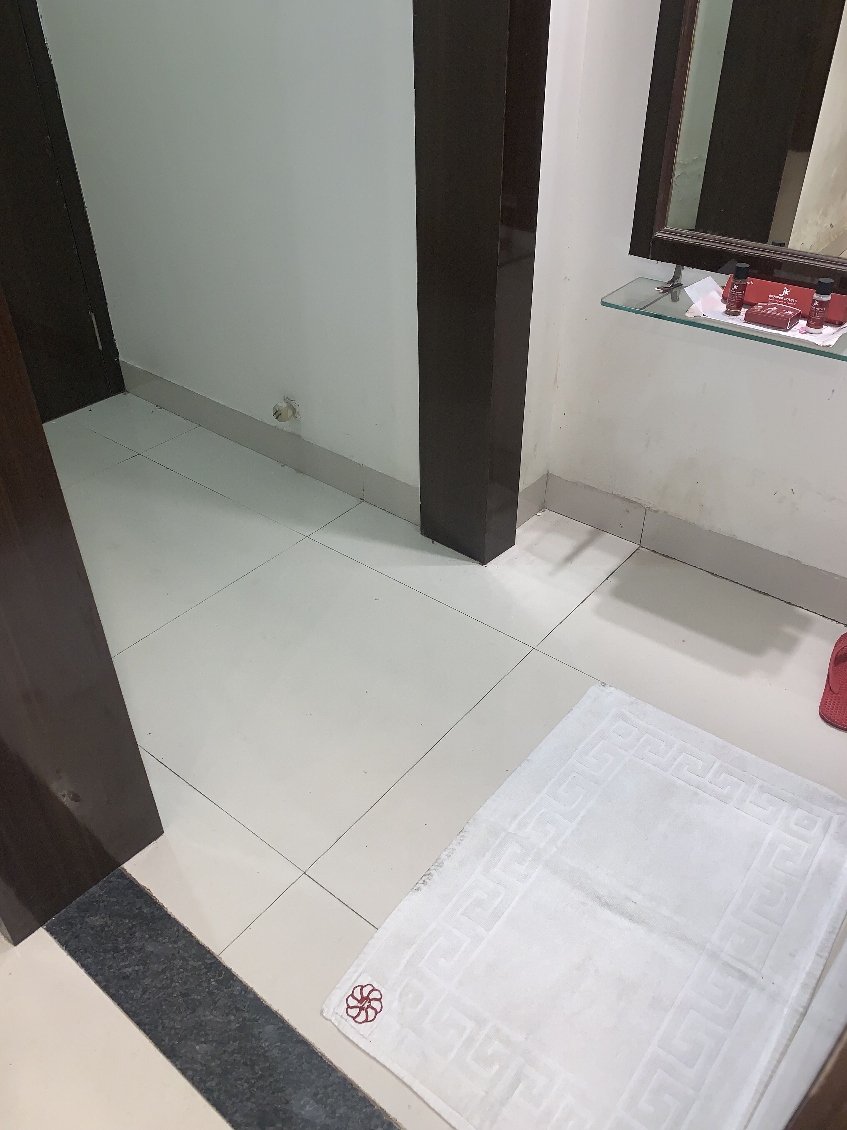 A room with a tiled floor, a white rug, a mirror, and a shelf with items.