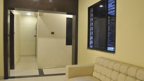 A room with a beige sofa, a window with a view, and a door leading to another room. - JK Rooms 126 Parashar Legacy - Station (Nagpur)
