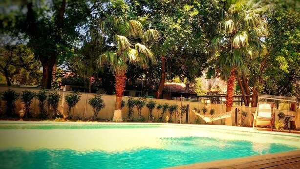 A swimming pool with a wooden deck, surrounded by palm trees and a concrete wall with climbing plants. - Dalyan Holiday Hotel (Ortaca)