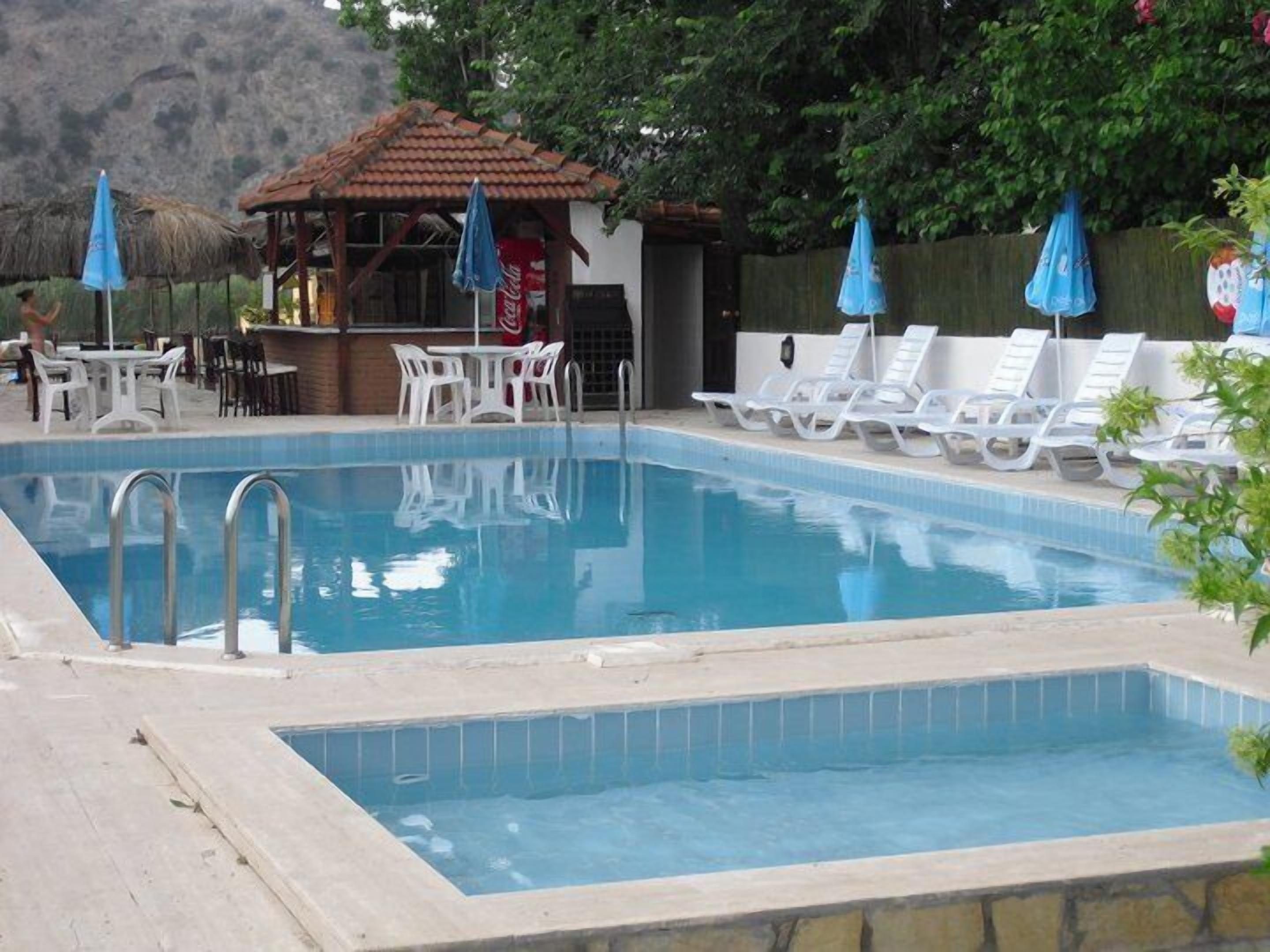A swimming pool with lounge chairs and umbrellas, a bar area, and a small hut.