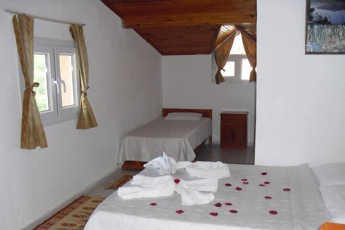 A bedroom with two beds, a wooden ceiling, and a window with curtains.