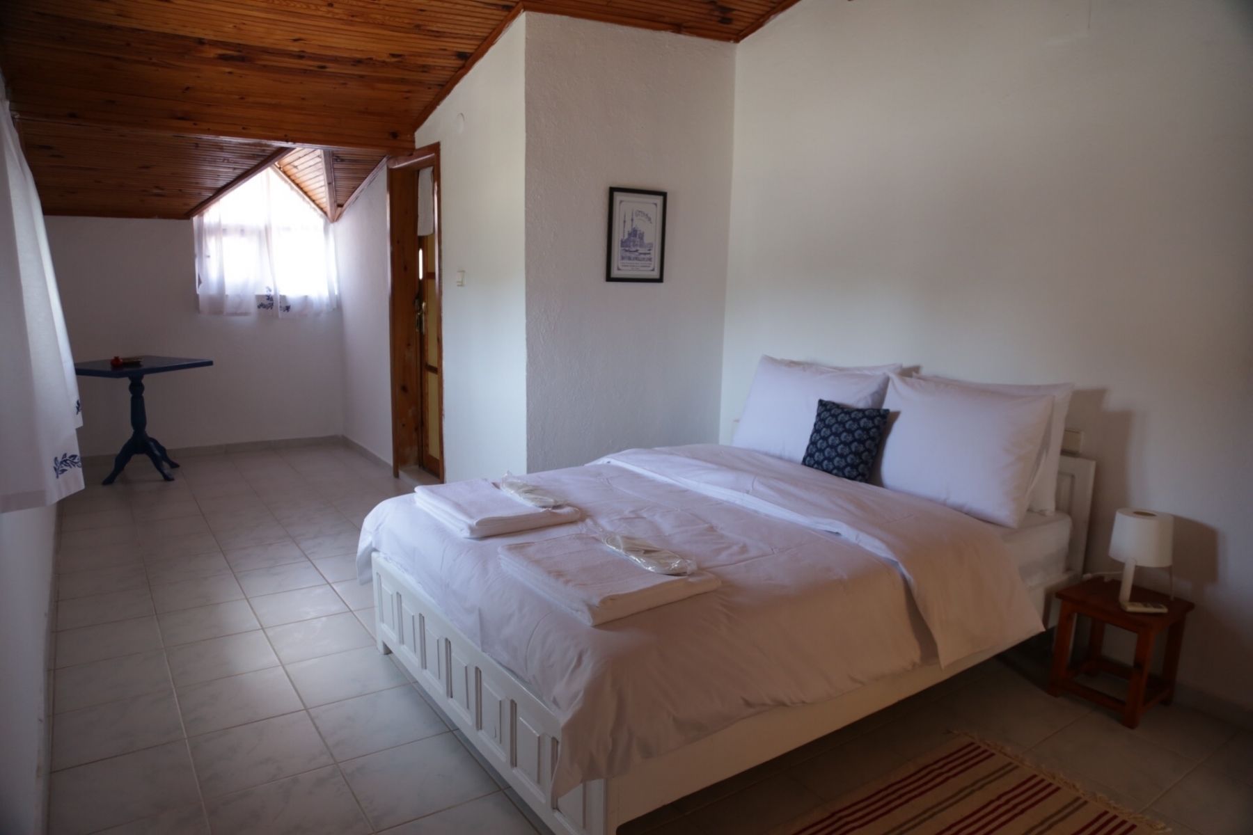Un dormitorio con una cama, una mesita pequeña y un cuadro en la pared.