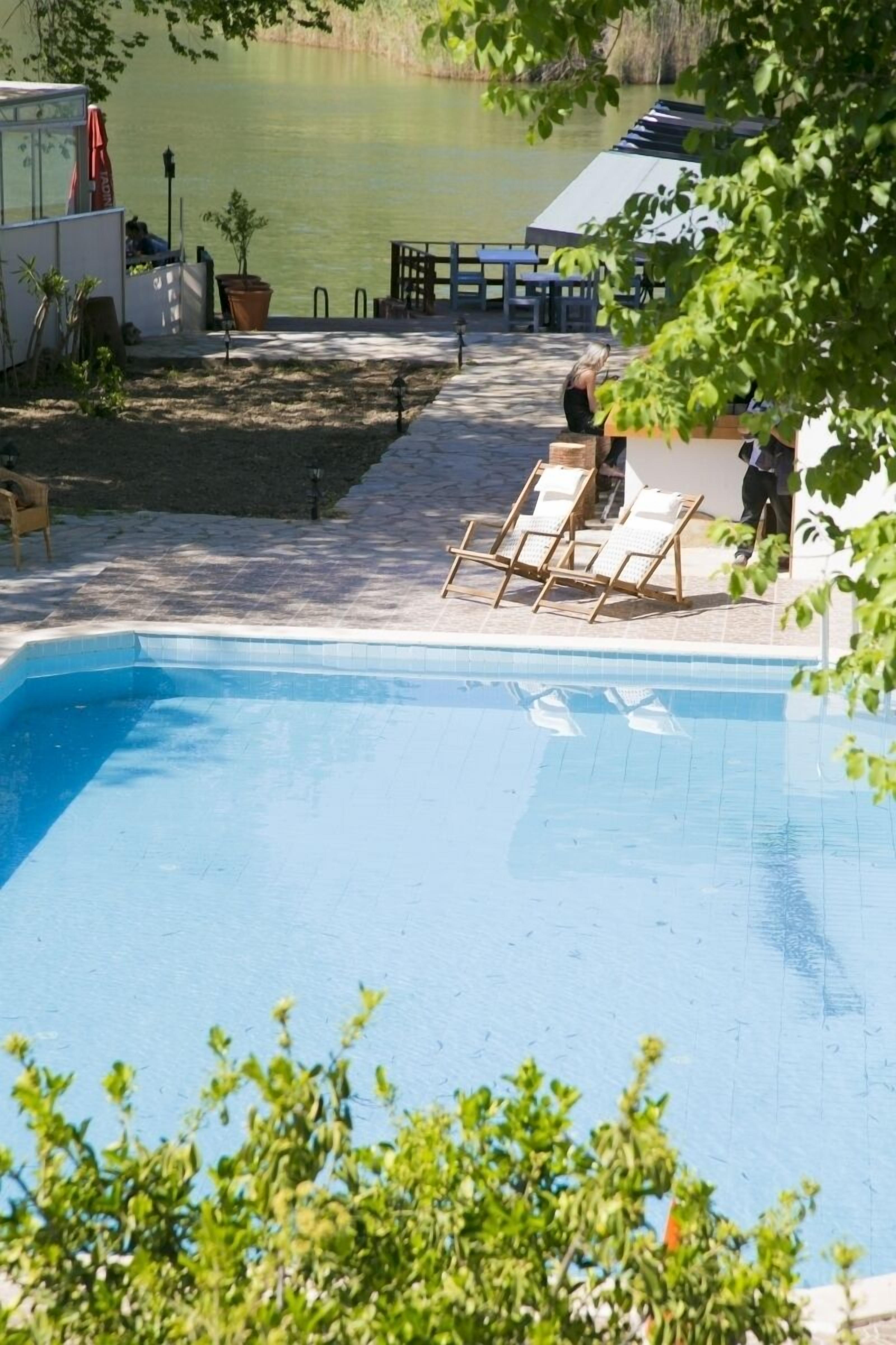 A swimming pool with lounge chairs, a small deck area, and a view of a lake.