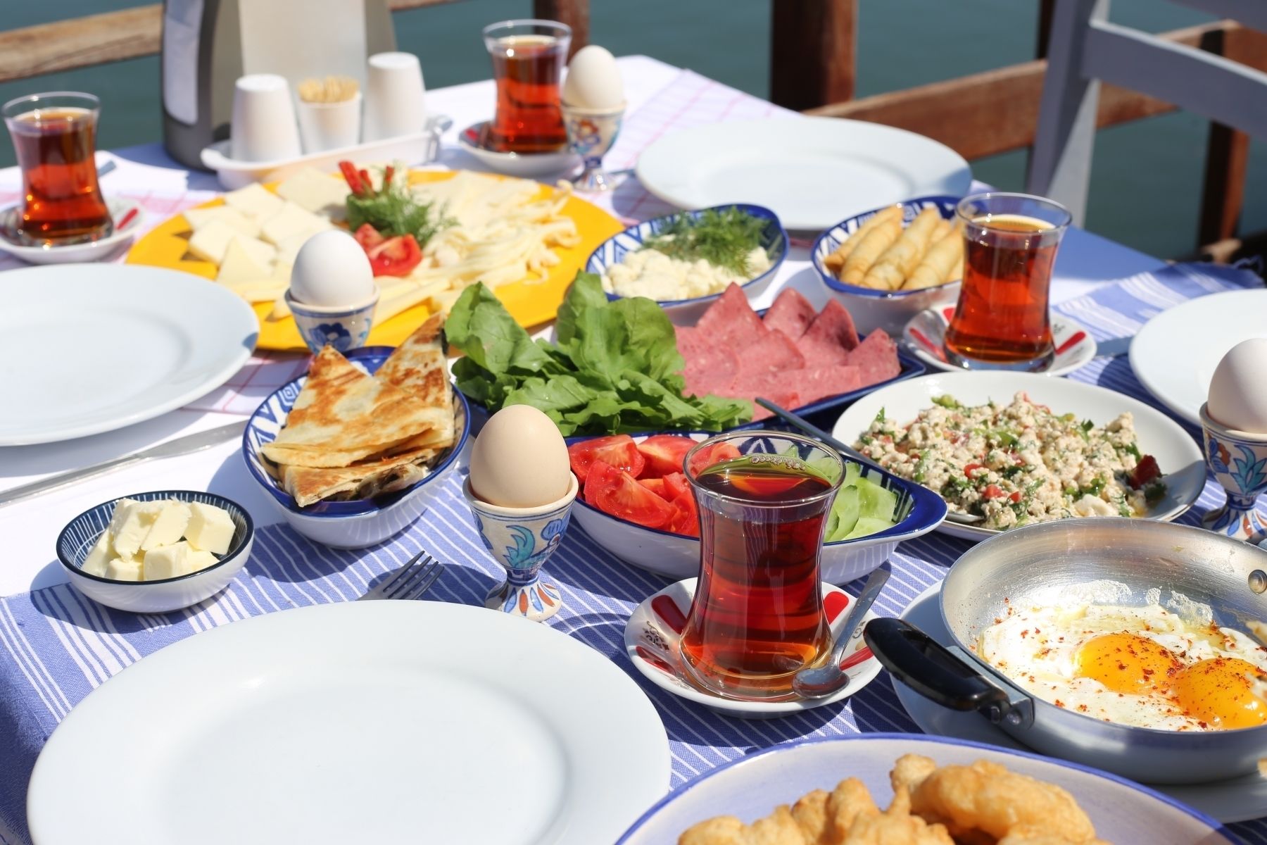 A table set with various dishes including eggs, salads, and bread, with cups of tea and utensils.