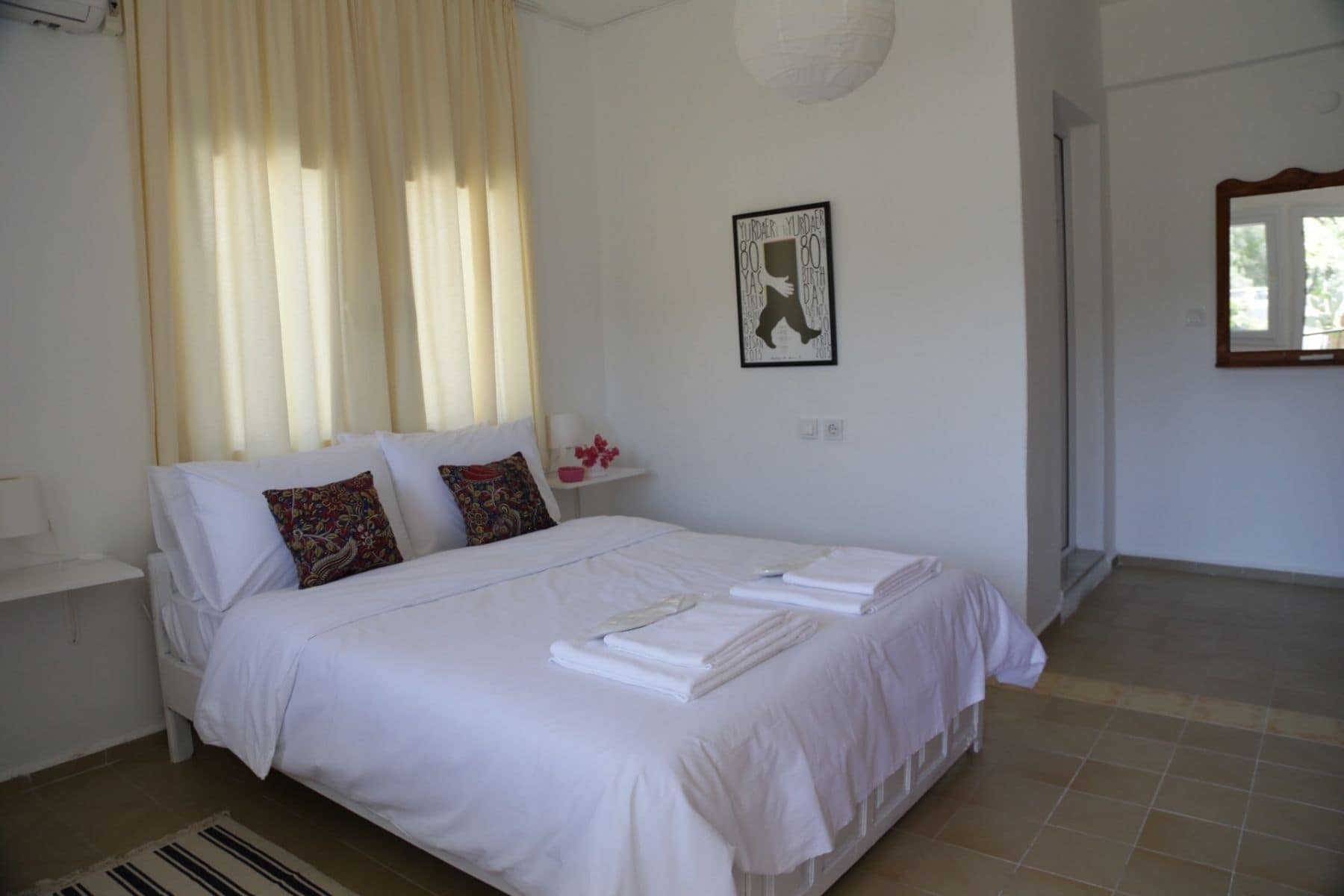 A neatly made bed with white linens and decorative pillows, a bedside table with a lamp, and a framed artwork on the wall.