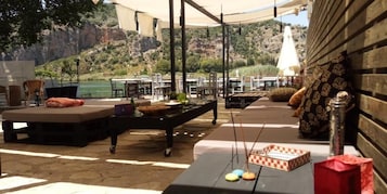 Un espacio al aire libre con mesas y sillas, una piscina y montañas al fondo.