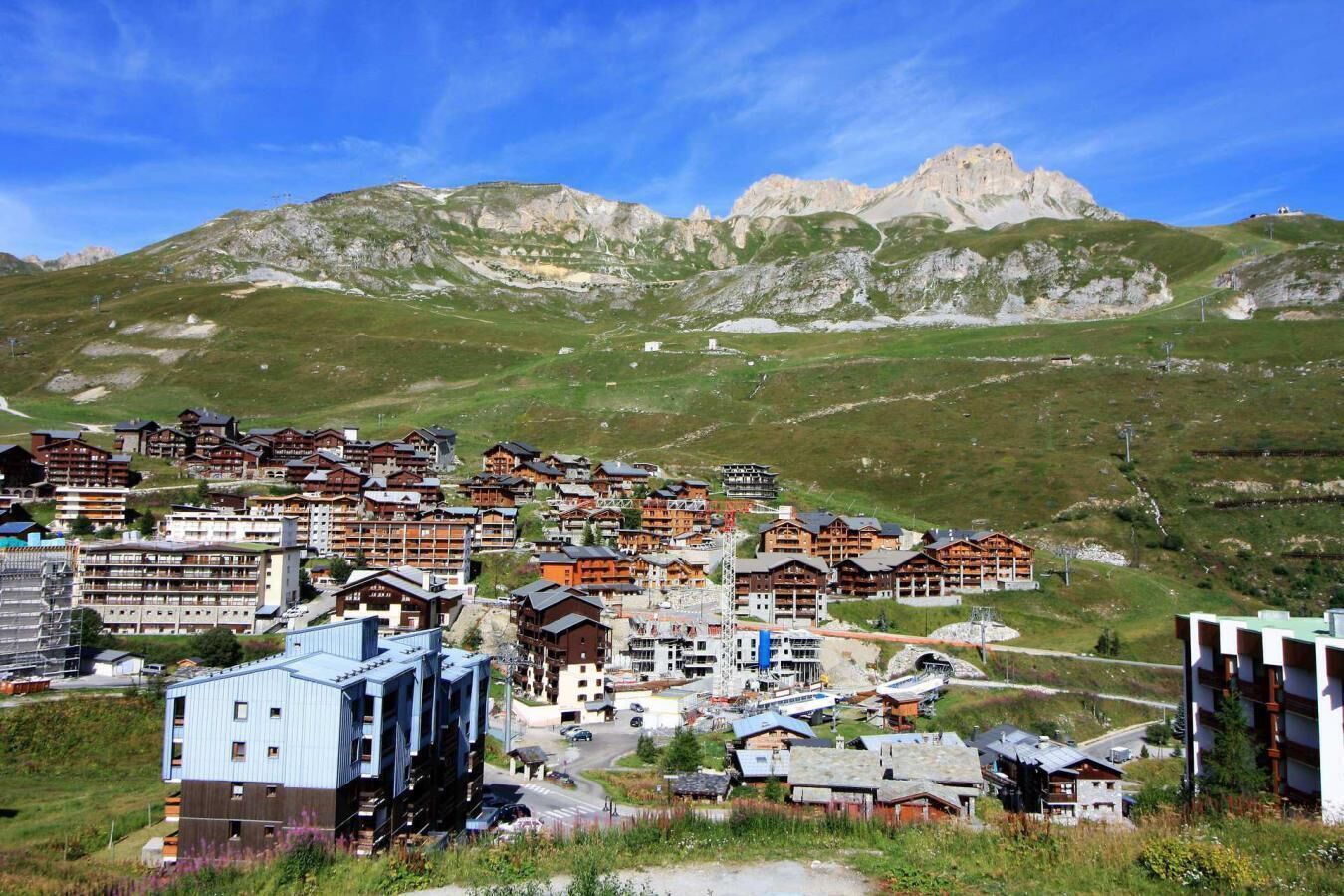 A mountainous resort town with traditional wooden buildings and modern structures, surrounded by lush green hills and rocky peaks.