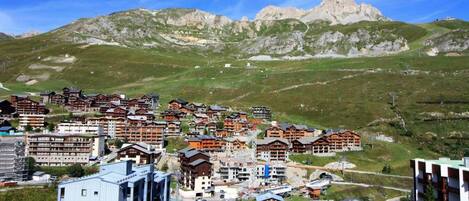 A mountainous resort town with traditional wooden buildings and modern structures, surrounded by lush green hills and rocky peaks.