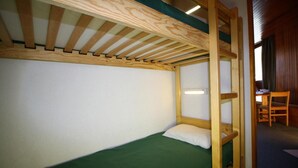Una cama litera con colchón verde y cabecera de madera, un escritorio con silla y una ventana con cortinas.