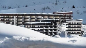Un conjunto de edificios modernos de varios pisos con balcones, con montañas nevadas al fondo.