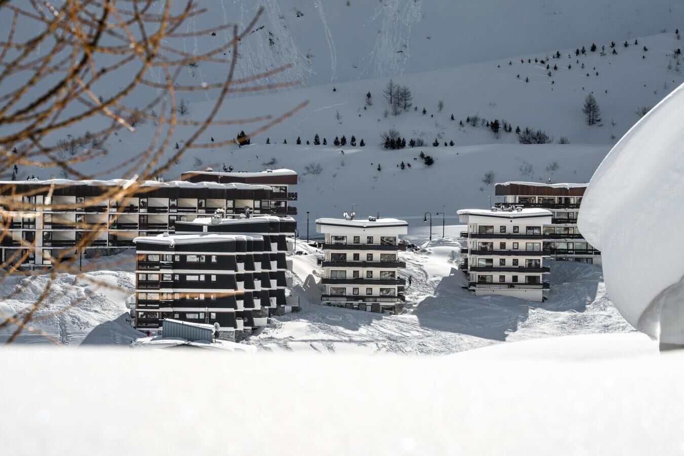 Une montagne enneigée, sur laquelle se dressent plusieurs bâtiments à étages, probablement des hôtels, dotés de balcons, et une piste de ski en arrière-plan.