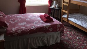 Un dormitorio con cama, literas, ventana con cortinas, televisor de pantalla plana y una mesita con taza y platillo.