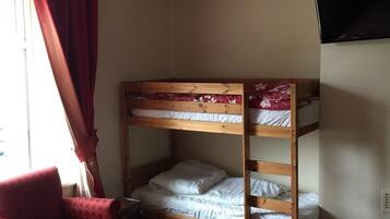 A room with a bunk bed, a red chair, a bed with a floral bedspread, and a television on the wall.