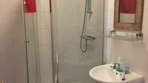 Un baño con ducha envuelta en vidrio, un lavabo blanco y un inodoro.