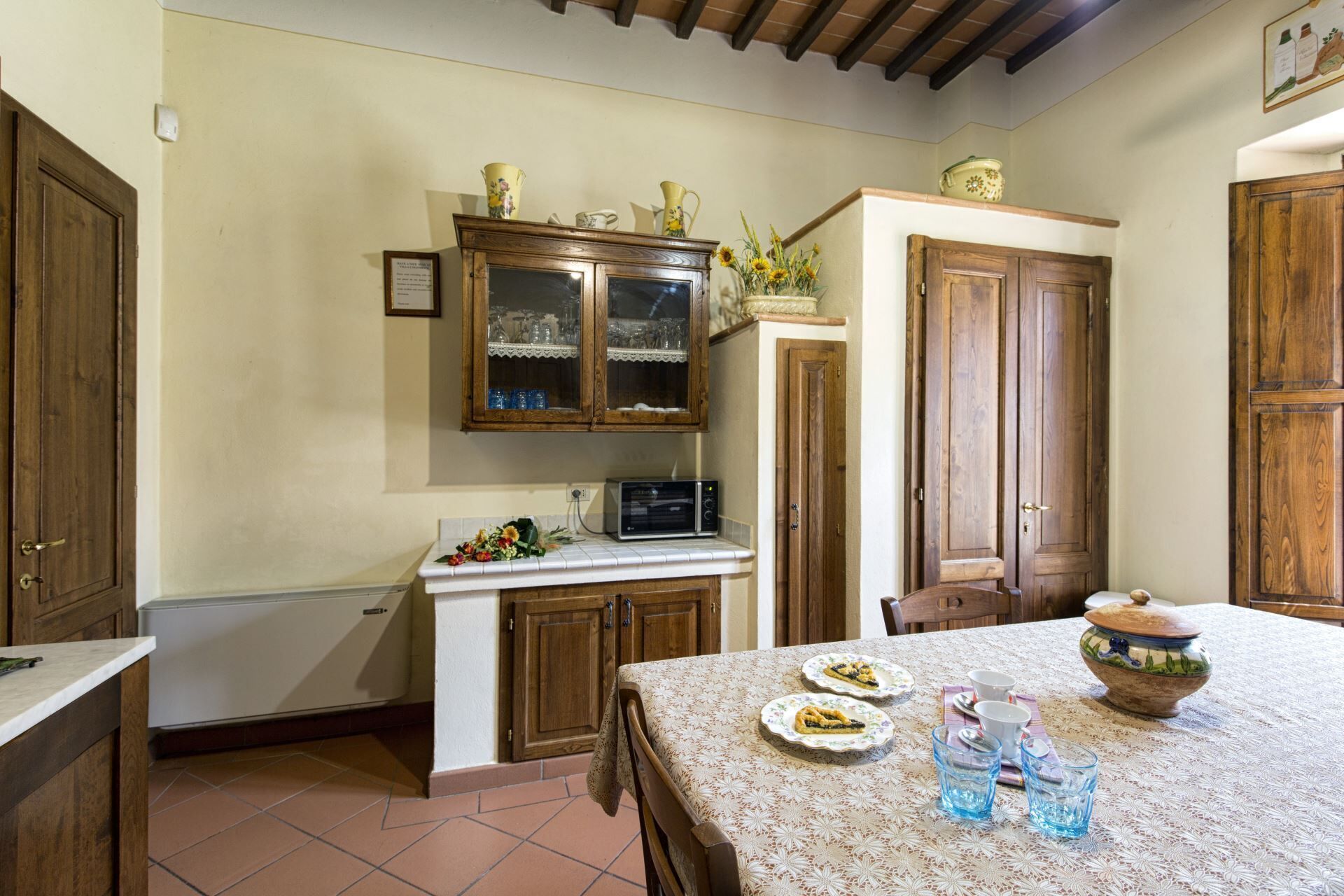 A kitchen with wooden cabinets, a microwave, and a table set with plates and glasses.