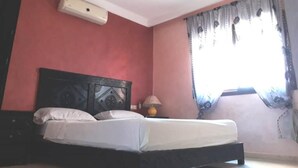 A bedroom with a bed, a nightstand, a lamp, and a window with curtains. - Charming little studio in Marrakech 4095 (Marrakech)