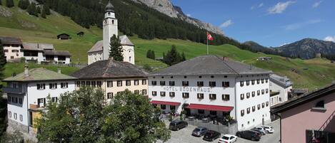 Un hotel con techo rojo y campanario, rodeado de un estacionamiento y vegetación.