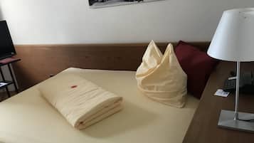 A neatly made bed with a folded blanket and a decorative pillow, a desk with a lamp and a telephone, and a wall-mounted picture.