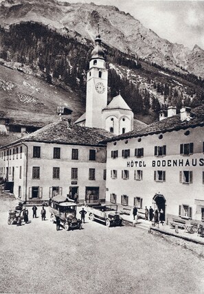 Un hotel histórico con una imponente torre de reloj, rodeado de terreno montañoso.