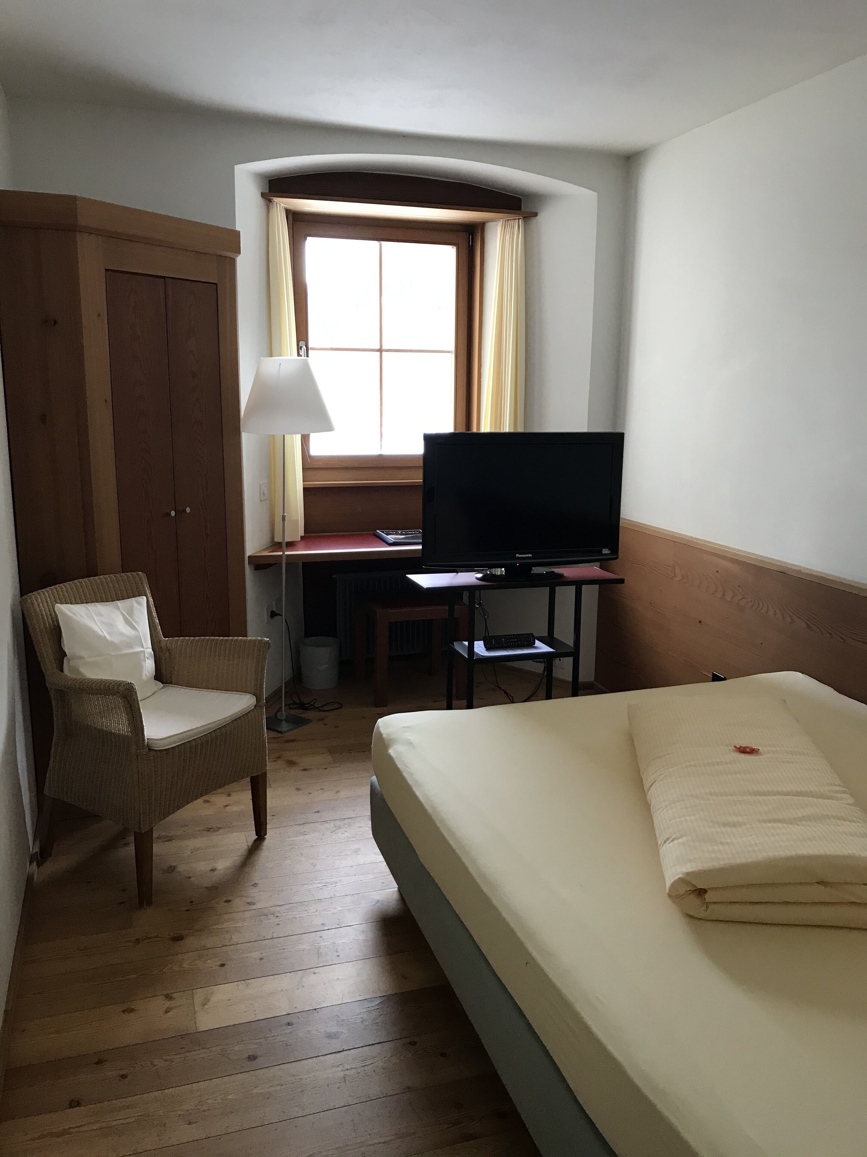Habitación de hotel con cama, una silla, escritorio y televisión, además de una ventana con cortinas.