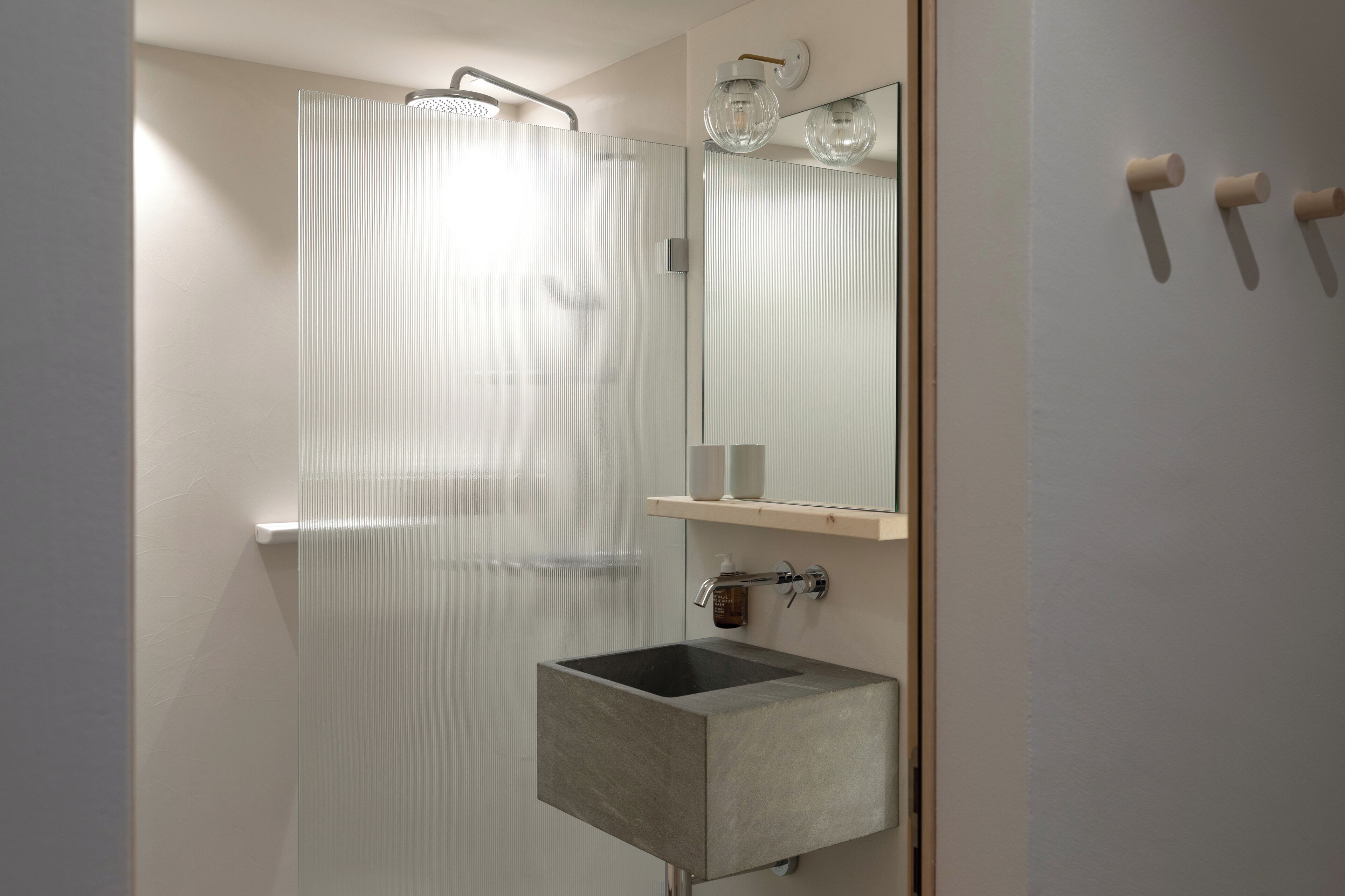 A modern bathroom with a glass shower enclosure, a built-in sink, and a mirror with a shelf above.