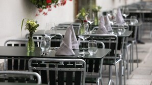 A row of tables with metal chairs, each set with a glass, a folded napkin, and a small vase with flowers. - Hotel Bodenhaus (Rheinwald)