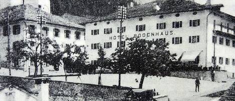 A historic building with a tower, a sign reading "Hotel Boenhaus," and a carriage on the street.