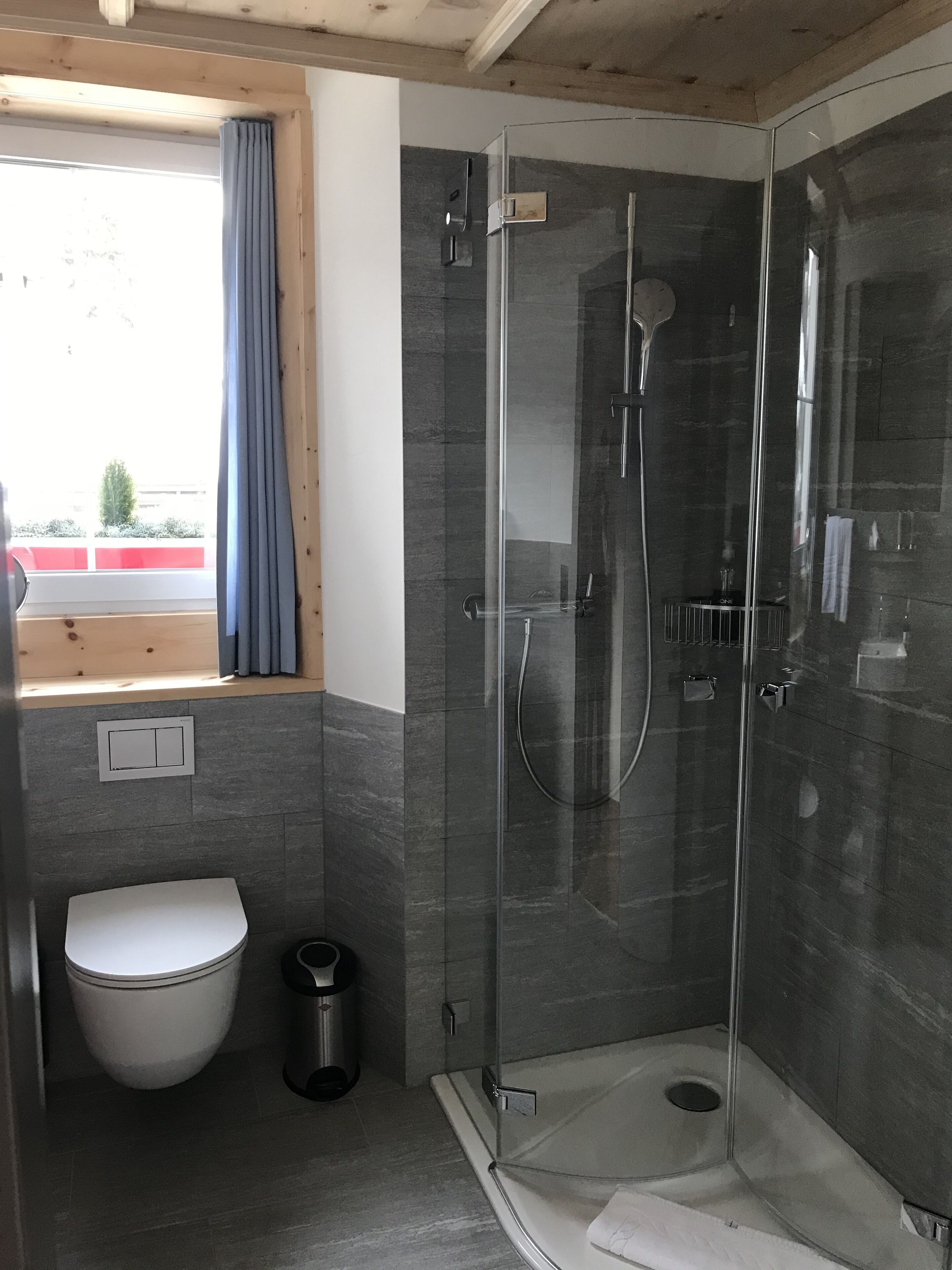 Un baño moderno con ducha envuelta en vidrio, inodoro y ventana con vistas al exterior.