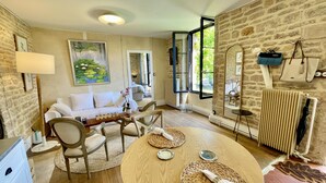 A cozy room with a stone wall, a wooden dining table with woven placemats, a white sofa, and a large window with a view of greenery. - Mon Coeur House and Garden designed by Stay in Beaune is a unique property  (Beaune)