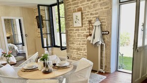 A dining area with a round table, white chairs, and a view of the outdoors through large windows. - Mon Coeur House and Garden designed by Stay in Beaune is a unique property  (Beaune)