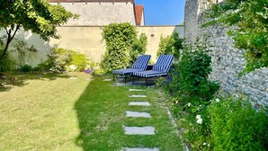 A garden with a stone wall, two striped lounge chairs, and a grassy area with stepping stones. - Mon Coeur House and Garden designed by Stay in Beaune is a unique property  (Beaune)