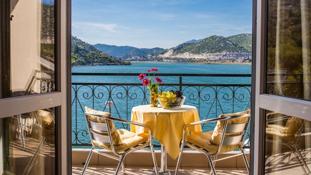 A balcony with a table and chairs, overlooking a body of water and hills.