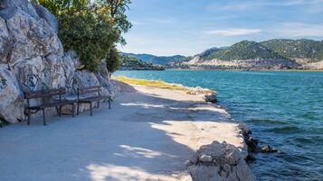 Un espacio con bancos frente al mar, con rocas al fondo y vistas a las colinas.